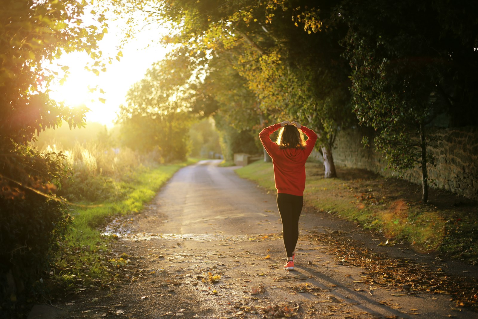 Woman walking briskly on a sunlit tree-lined path