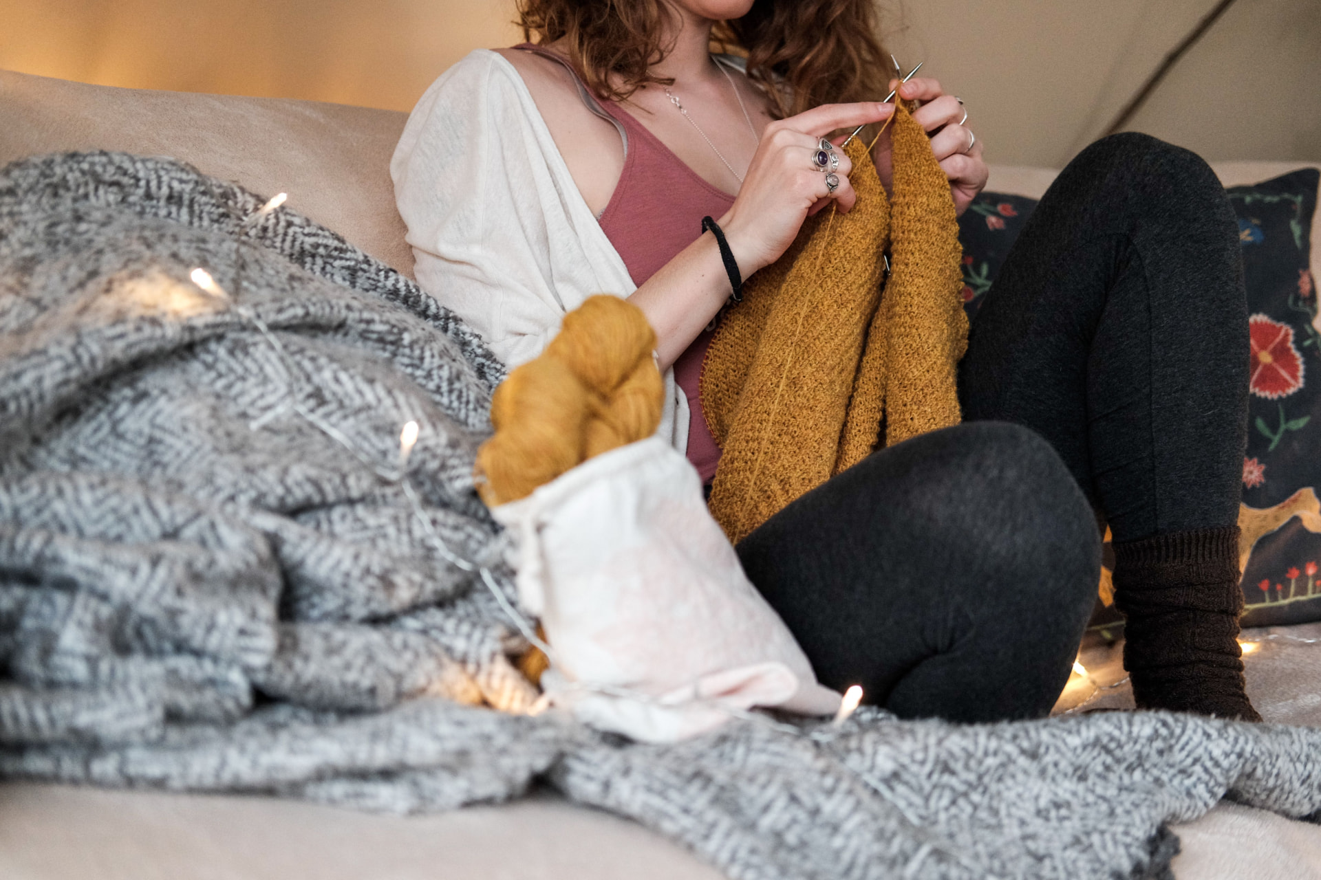Woman knitting on a sofa under warm string lights